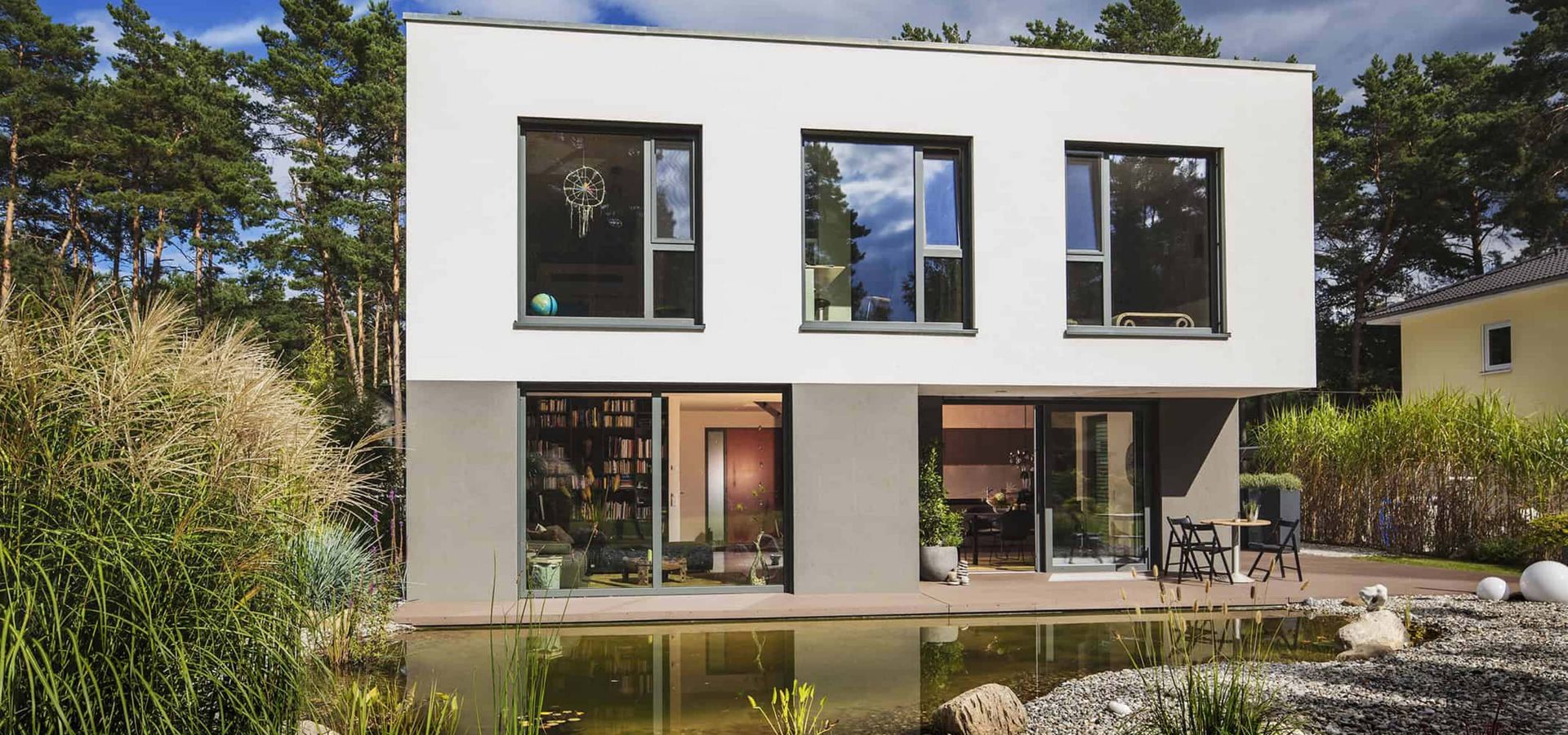 Modernes Haus mit einem Teich und einem gepflegten Garten im Vordergrund.